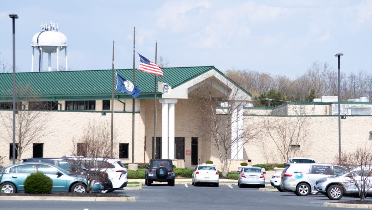A tan building with a green roof and cars in the parking lot