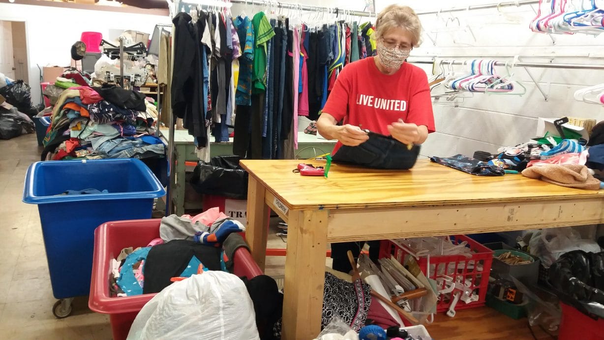 A volunteer wearing a mask sorts clothes in a cluttered room during a previous year's United Way volunteer event.