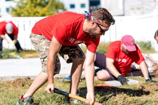 A man wearing a red shirt leans into his shovel during a United Way volunteer day.
