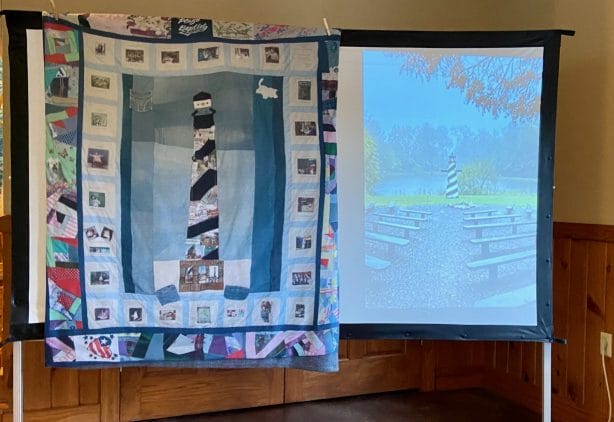 A quilt showing a lighthouse hangs on a whiteboard.