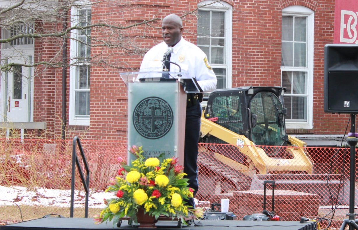 A man speaks from a podium in front of flowers