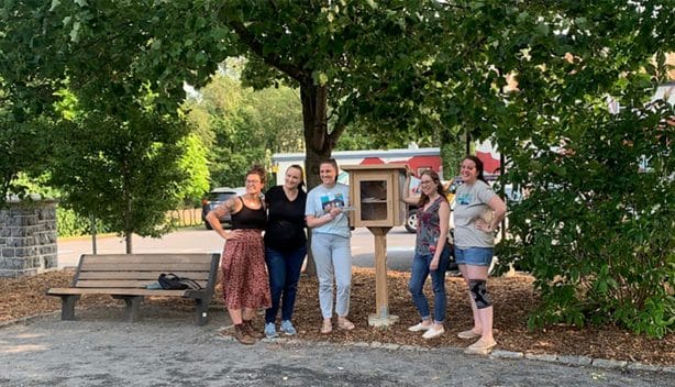 five women stand next to a small outdoor cabinet