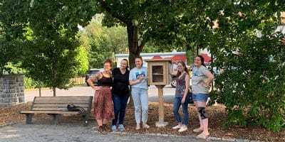 five women stand next to a small outdoor cabinet
