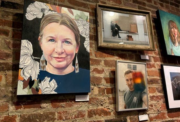 Three framed paintings and two photographs hanging on a brick wall