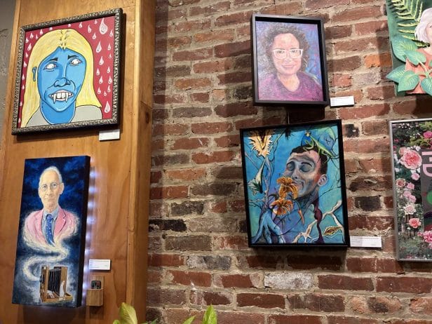 Six paintings hang on a brick wall