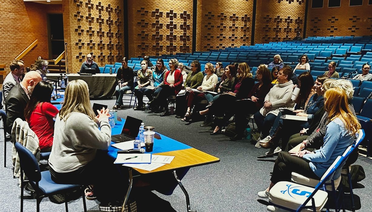 people sitting in auditorium seats facing a table with others