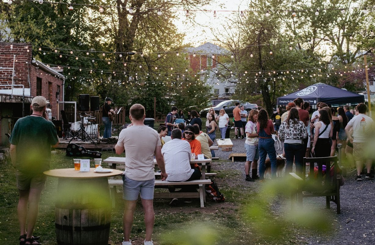 people in an outdoor space listening to a person playing guitar