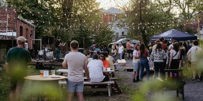 people in an outdoor space listening to a person playing guitar