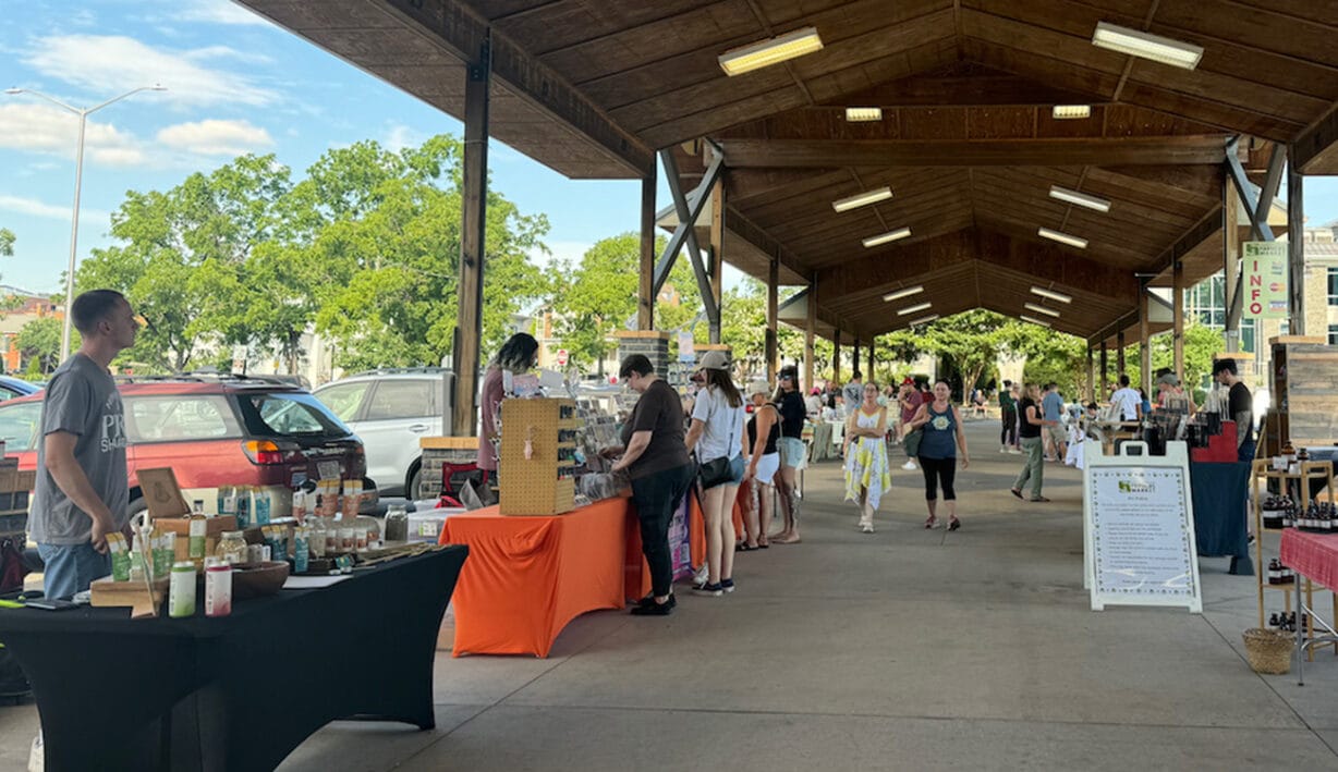 People walking past tables with food and goods