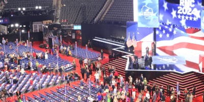 people standing around empty seats in front of a big stage with a digital screen