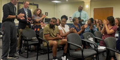 Four people standing while two dozen others sitting clap