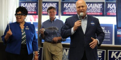 A woman and two men stand in front of blue and white campaign signs.