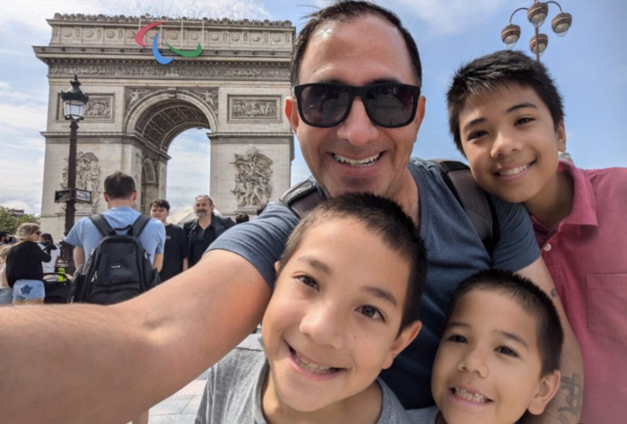 A man taking a selfie with three children in front of the Arc De Triomphe in Paris.