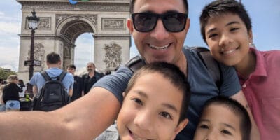 A man taking a selfie with three children in front of the Arc De Triomphe in Paris.