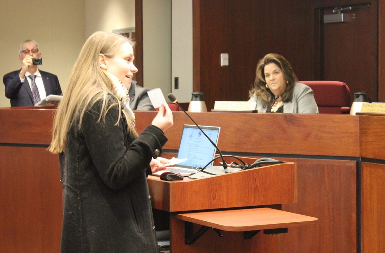 A woman a podium holds a slip of paper