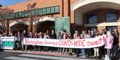 a group of people holding a long homemade sign saying "Rockingham deserves COUNTY-WIDE transit"