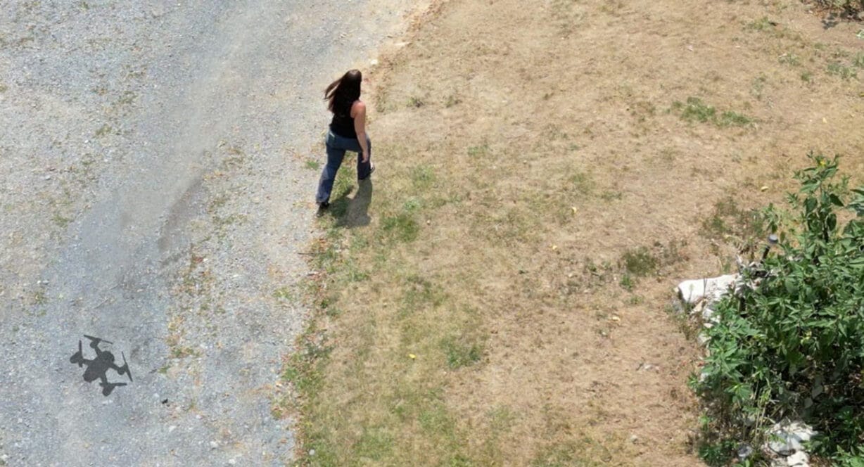 A photo taken from above showing a shadow of a drone behind a woman. 