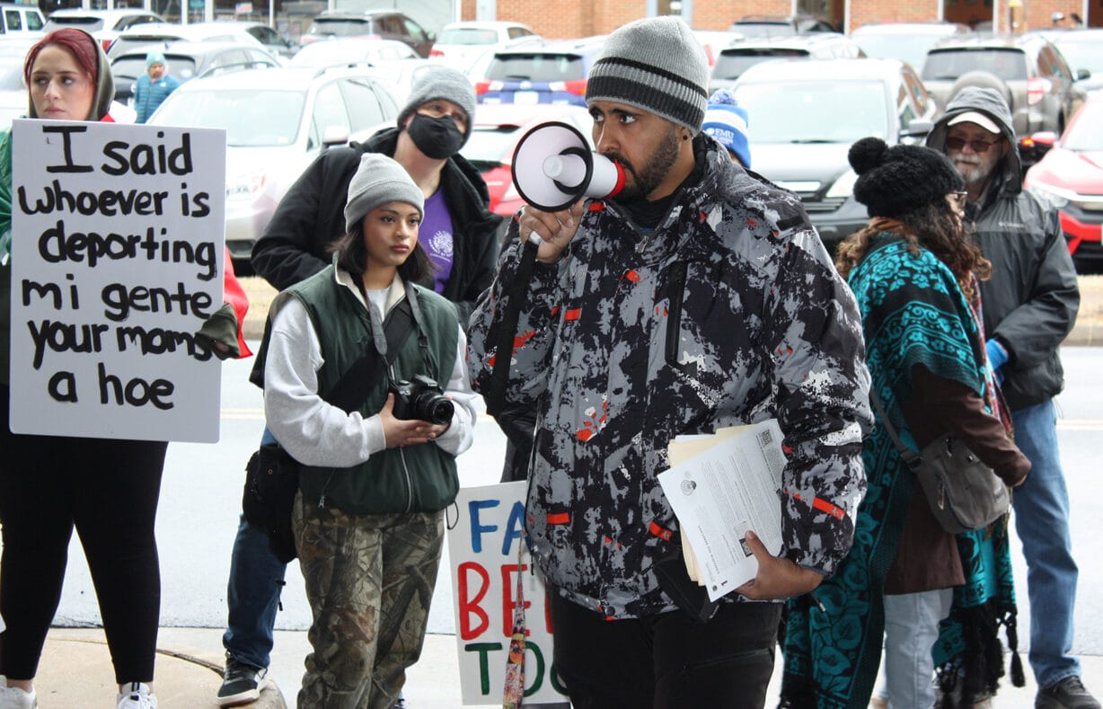 A man with a megaphone speaks in front of people with signs