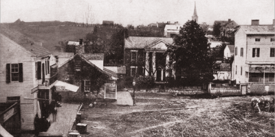 A black-and-white photo of old houses connected by a dirt road