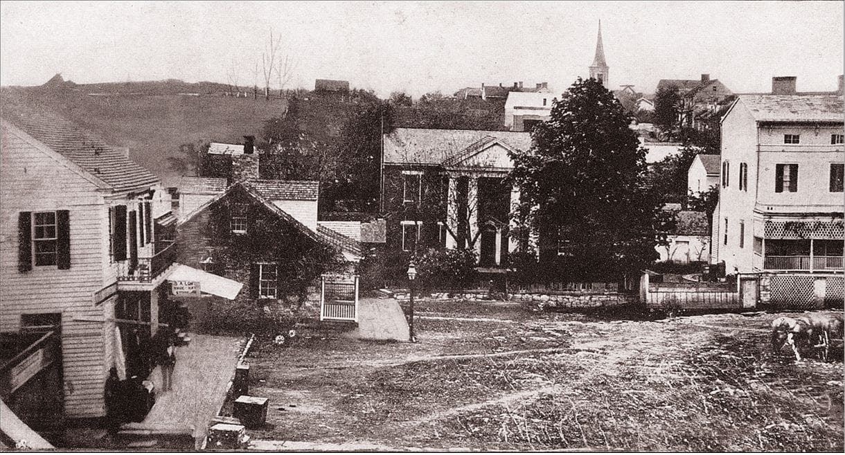 A black-and-white photo of old houses connected by a dirt road