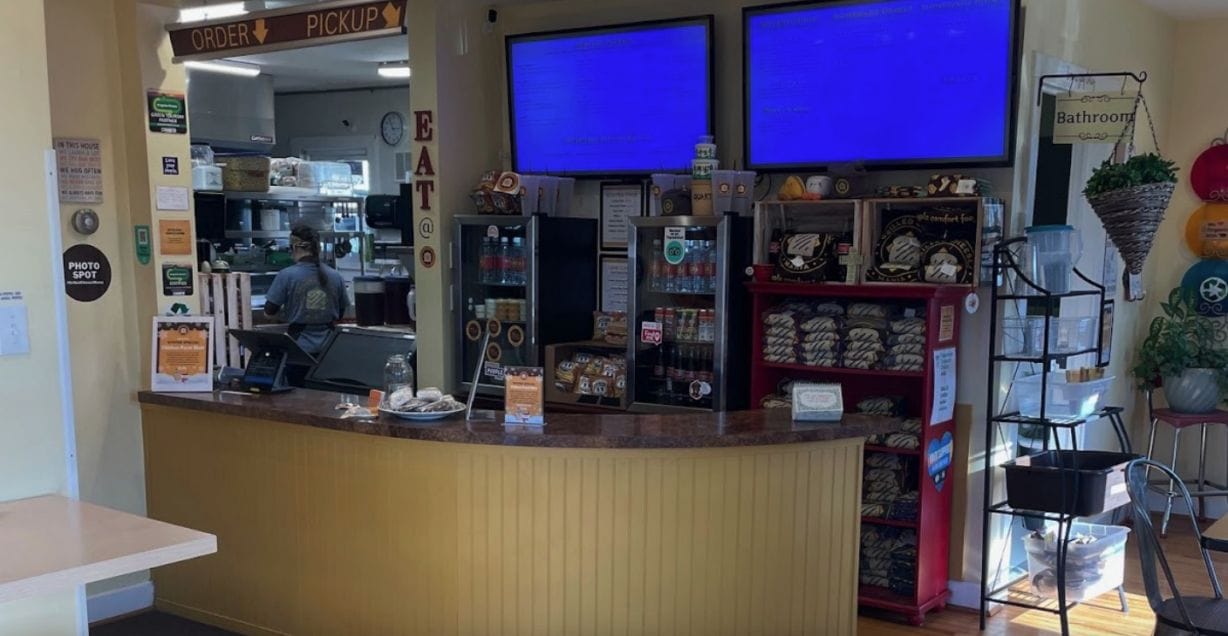 A lunch counter, menu board and peak into the kitchen where an employee is preparing an order