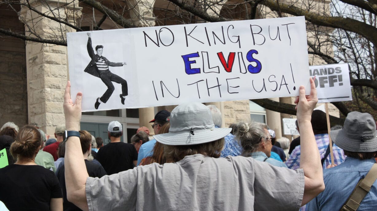 A man carries a sign that says "No King but Elvis in the USA"