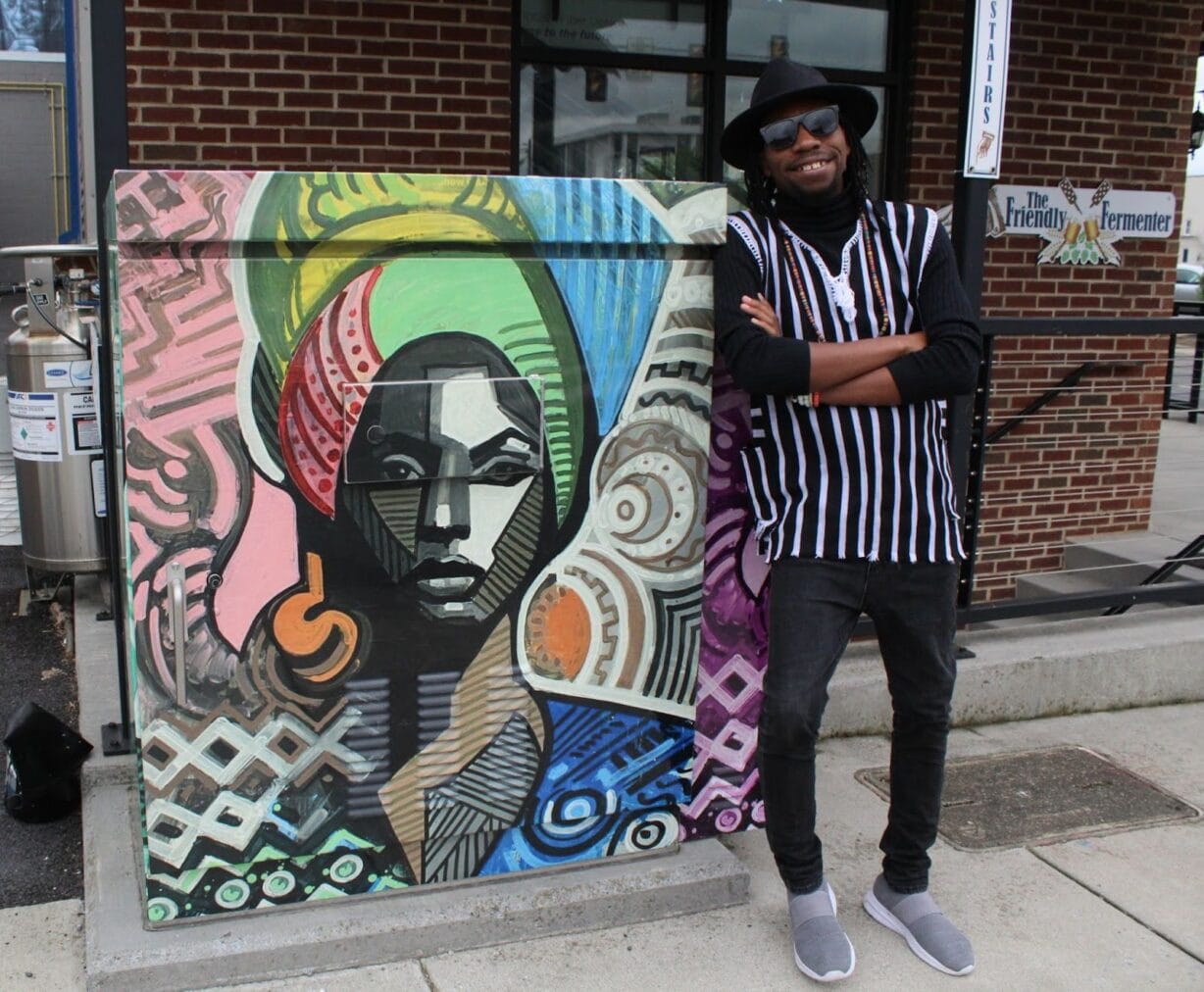 A man stands with his arms crossed and smiling next to a mural of a colorfully dressed woman