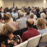 rows of chairs with people in every one in the city council chambers