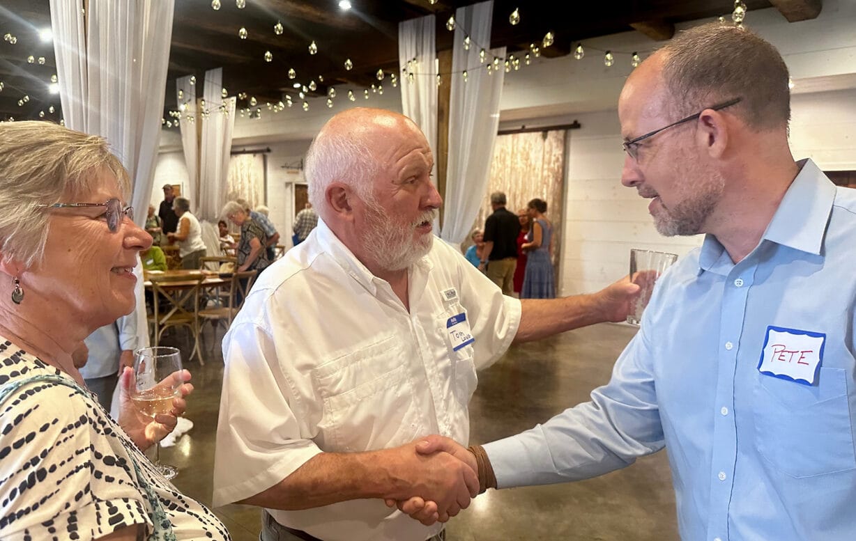 Two men shake hands while a woman in the left of the frame looks on