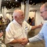 Two men shake hands while a woman in the left of the frame looks on