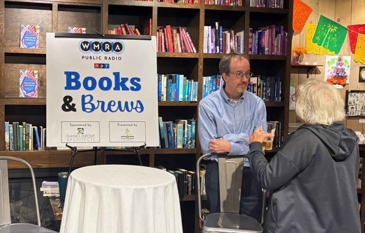 A man next to a "Books and Brews" sign speaks to a woman