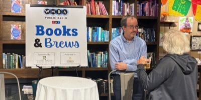 A man next to a "Books and Brews" sign speaks to a woman