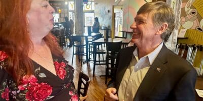 A man in a sport coat laughs while talking to a woman in a flowered dress