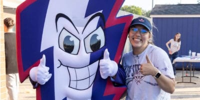 A woman gives a thumbs up next to a mascot, who is giving both thumbs up.